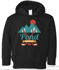 A black toddler pullover hoodie featuring a graphic design on the chest with mountains, pine trees, a sun, crossed hockey sticks, and the text 'Pond Hockey'.